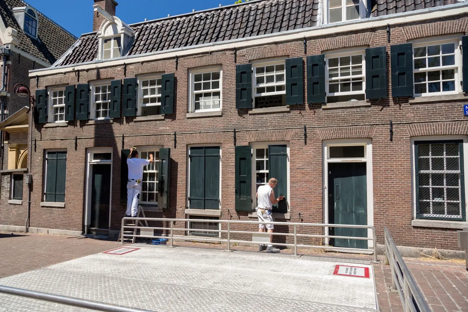 Schilders werken aan de kozijnen en luiken van de gevel van een Nederlandse bakstenen woning tijdens buitenschilderwerk